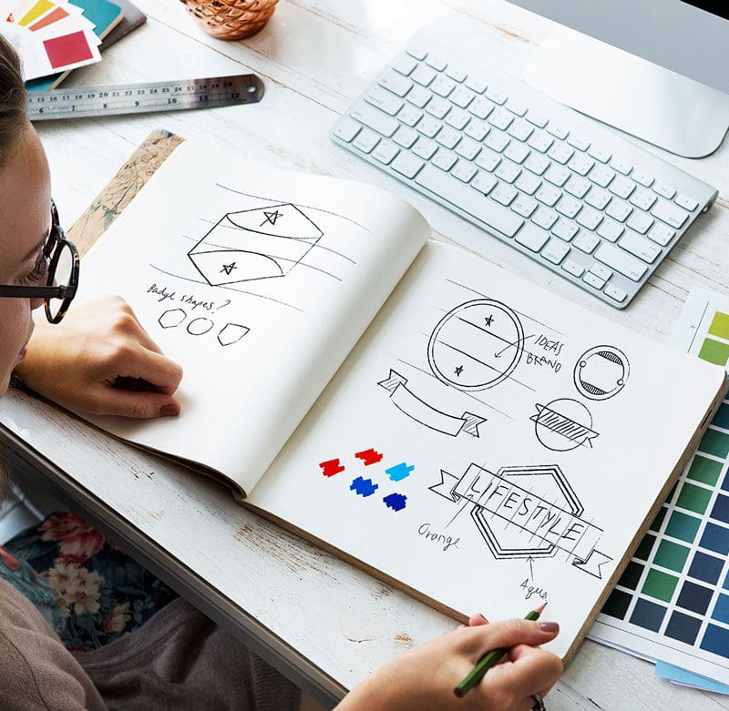 Graphic designer sketching brand identity concepts and logo ideas with color palette samples on desk