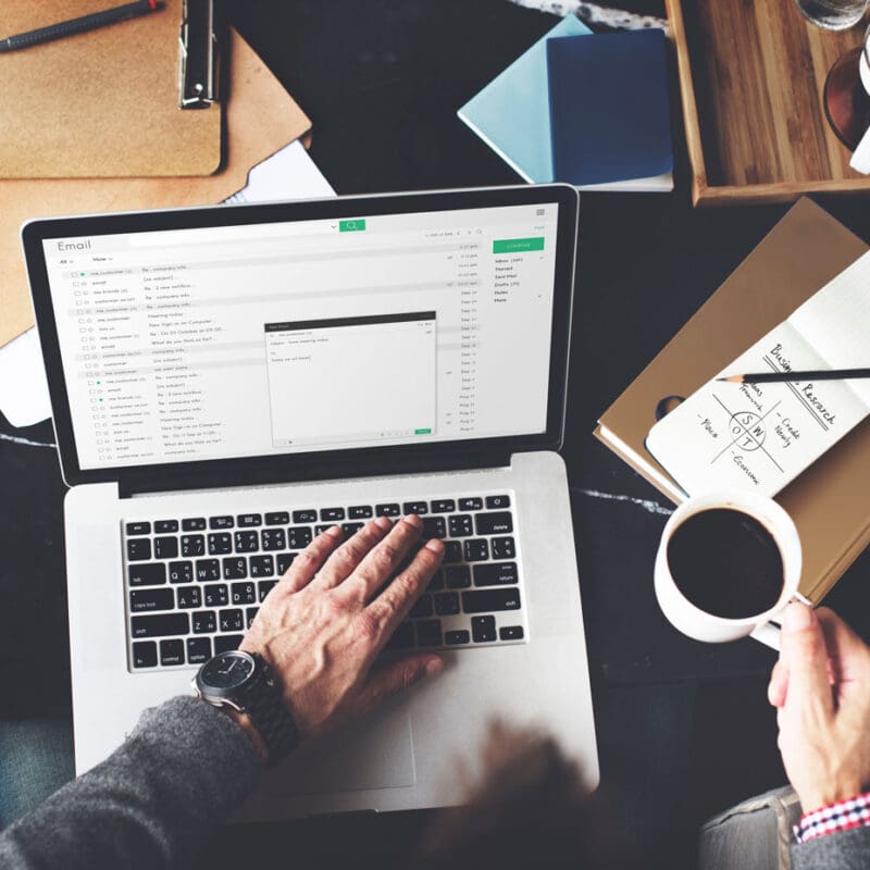 Person working on email marketing strategy at a desk with a laptop, coffee, and notes on branding and audience research.