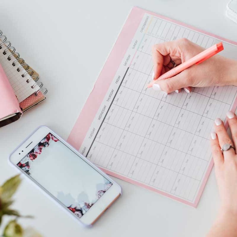 Person writing in a social media content calendar beside a smartphone and planner on a desk