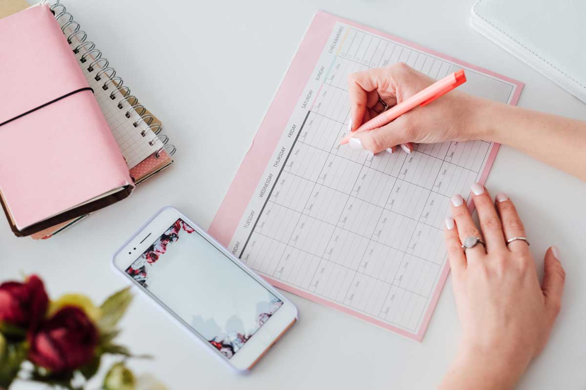 Person writing in a social media content calendar beside a smartphone and planner on a desk