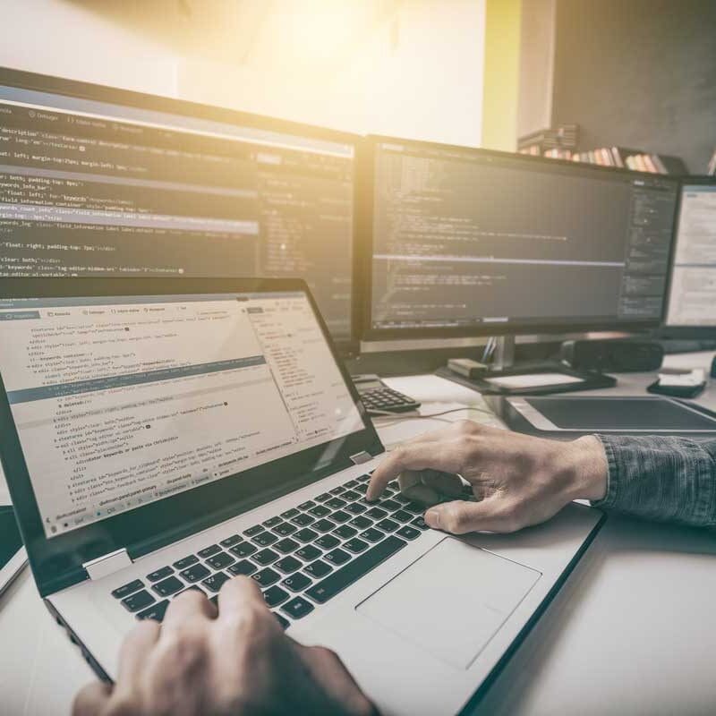Developer working on a laptop with multiple monitors displaying website code