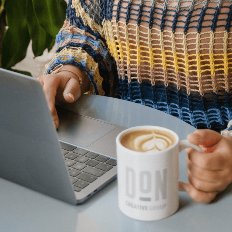 Creative professional working on laptop with Don Creative Group coffee mug in modern workspace