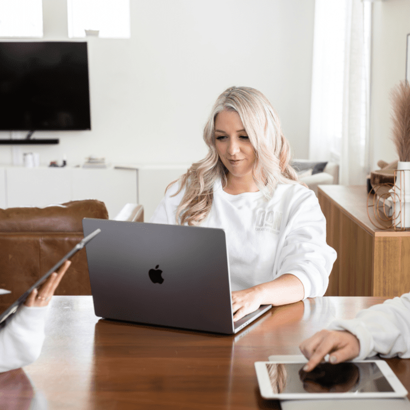 Three women from Don Creative Group collaborating at a table using laptops and tablets in a bright, modern workspace.