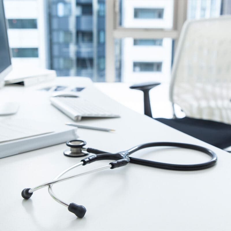 Stethoscope resting on a modern medical office desk with computer and chair in the background