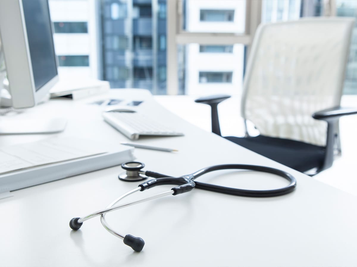 Stethoscope resting on a modern medical office desk with computer and chair in the background