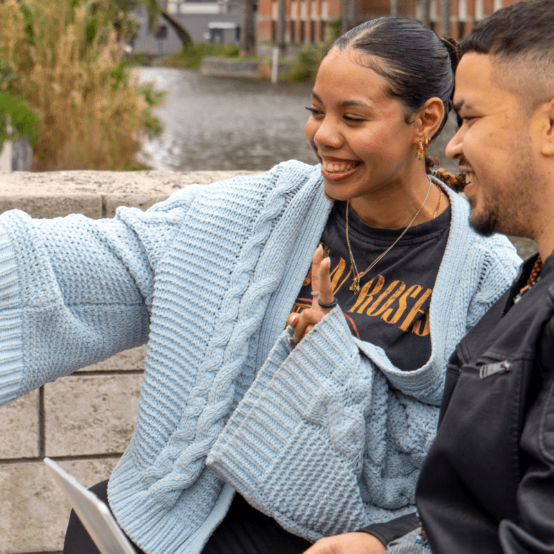 Two people smiling while taking a selfie outdoors, capturing a shared moment for social media content