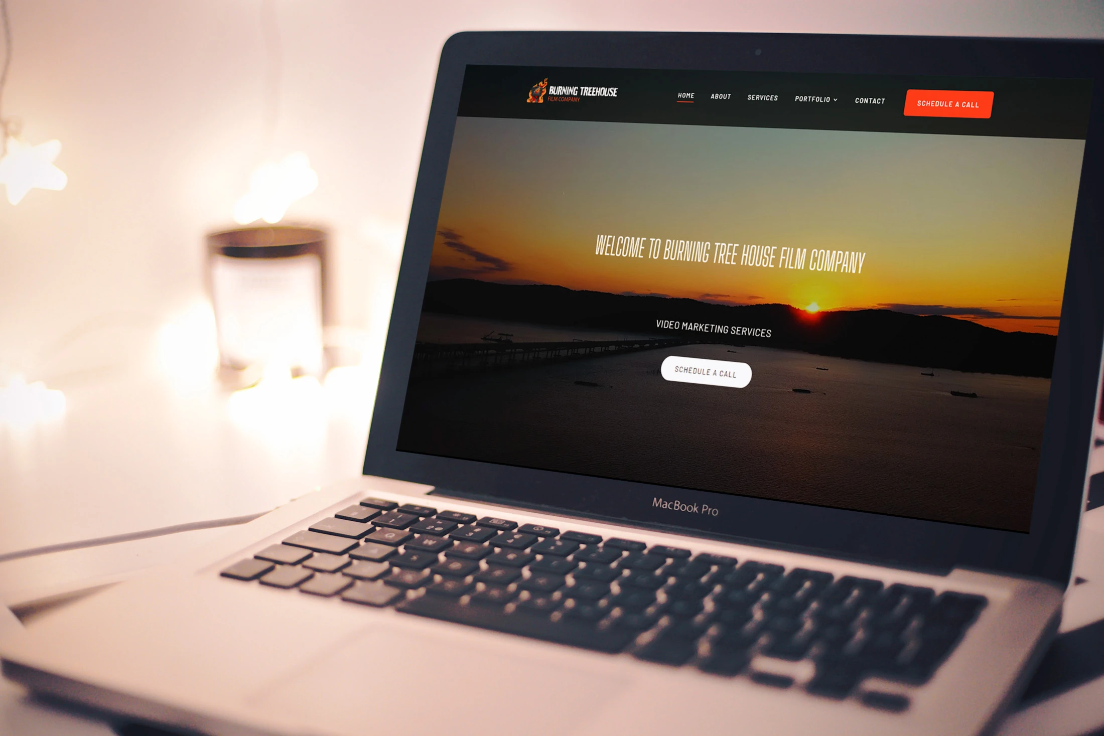 Laptop displaying the homepage of Burning Tree House Film Company with a sunset background and call-to-action button for video marketing services.