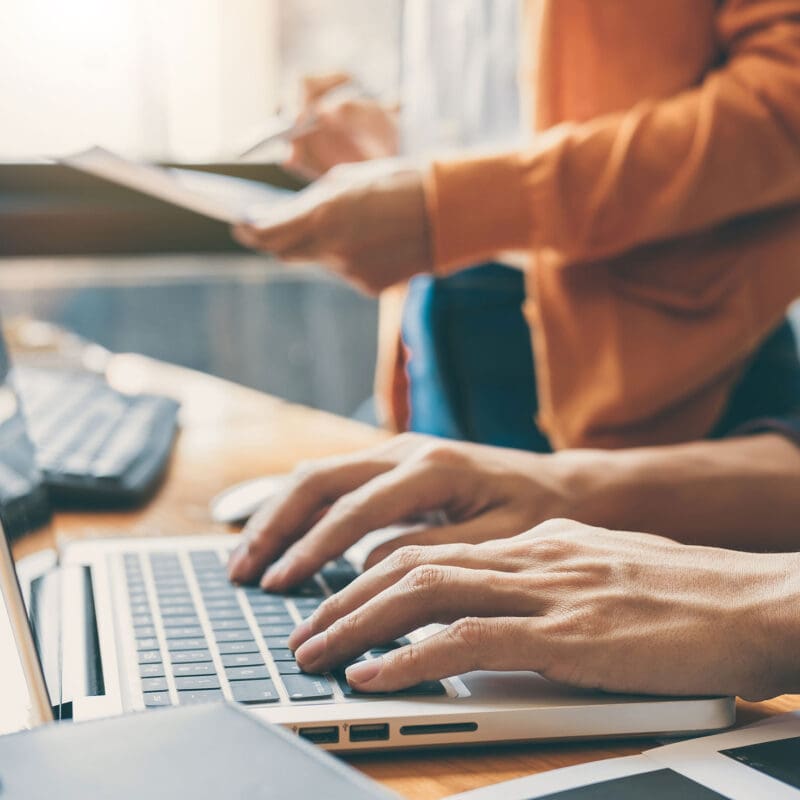Team members collaborating at a desk while working on a laptop and reviewing documents