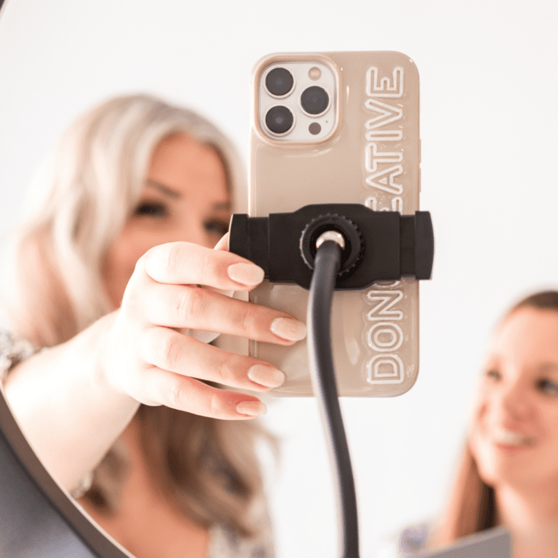 Two women setting up a smartphone in a ring light for content creation, with a custom Don Creative Group phone case in focus.