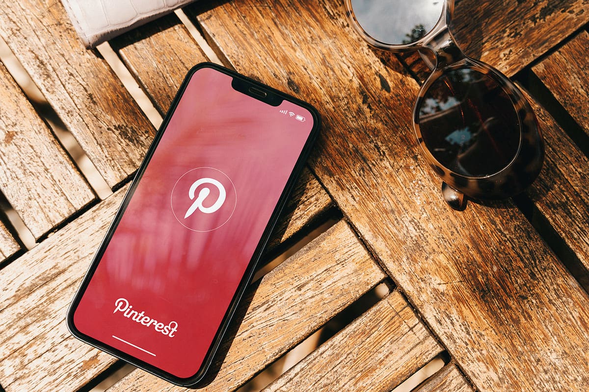 A phone on a table with the Pinterest login page, there is sunglasses next to the phone