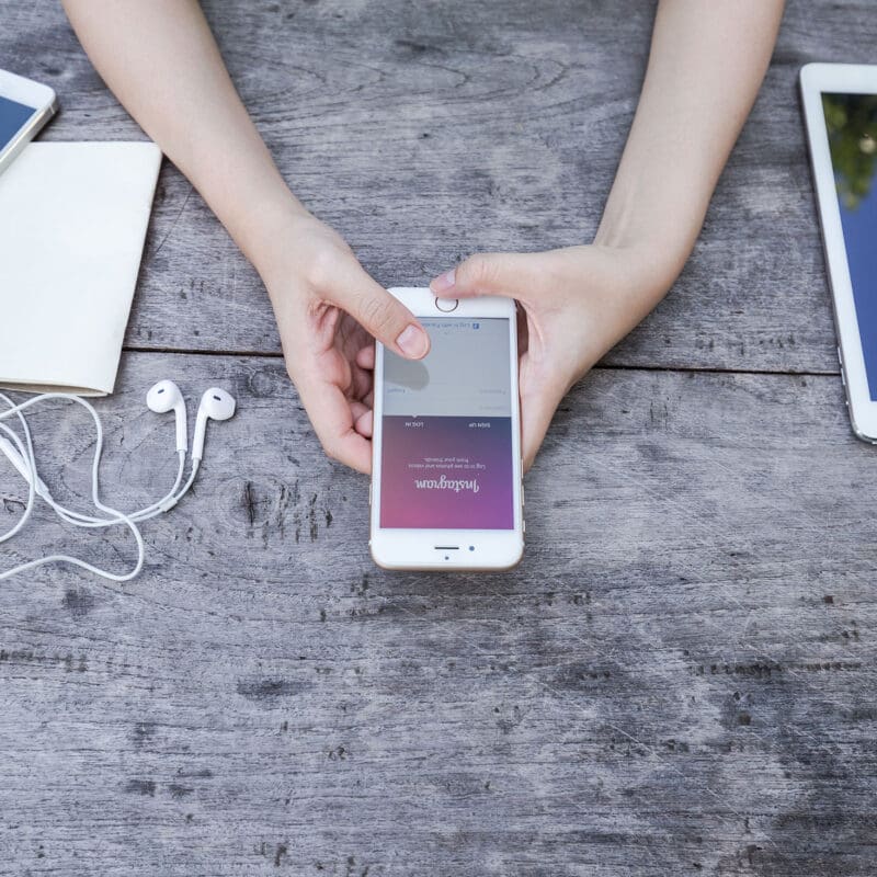 Hands holding a smartphone on a wooden desk surrounded by mobile devices and accessories