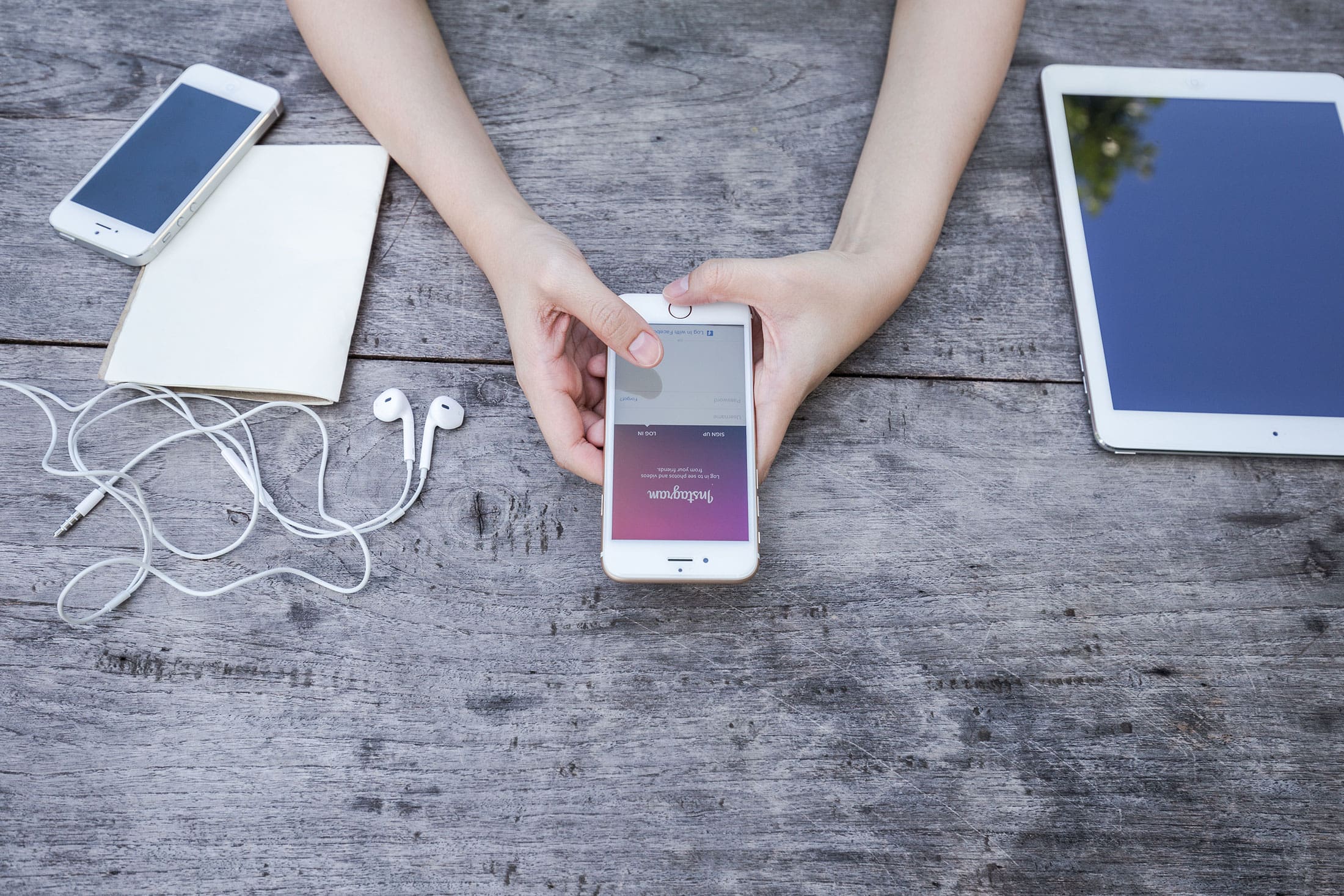 Hands holding a smartphone on a wooden desk surrounded by mobile devices and accessories