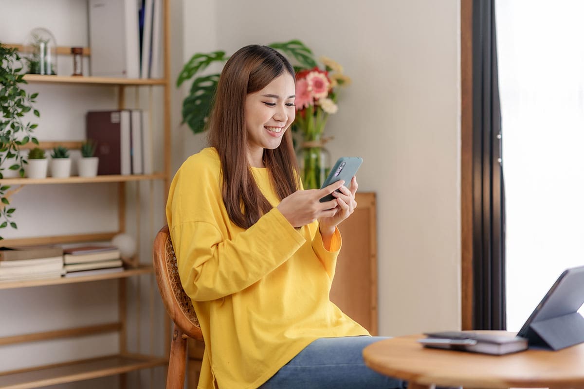 A woman smiling at her phone and working with a yellow sweater on