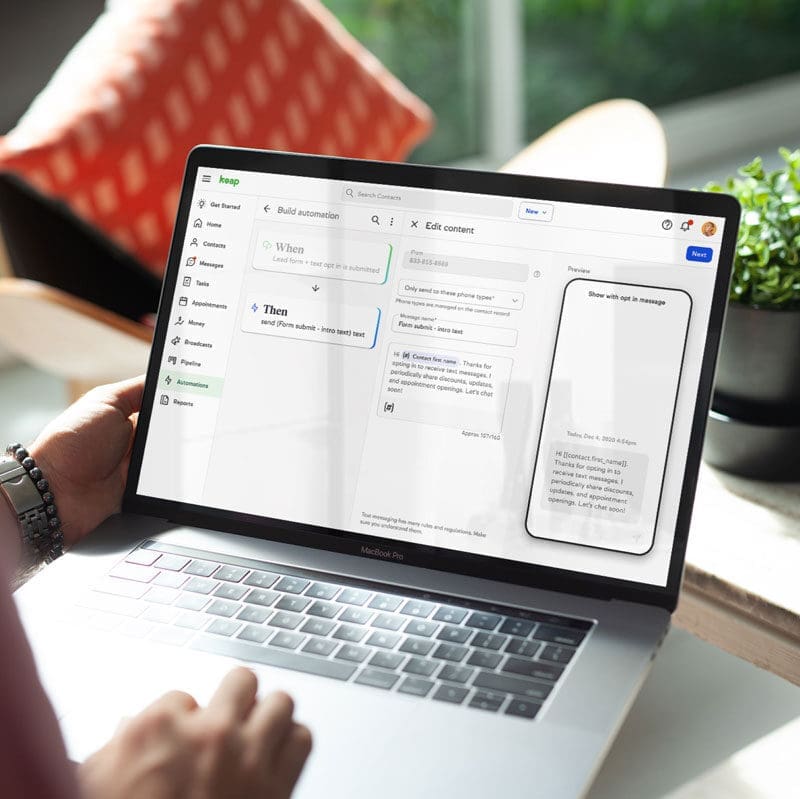 Person using a MacBook Pro to build an automation workflow in Keap CRM software, with a plant and window light in the background.