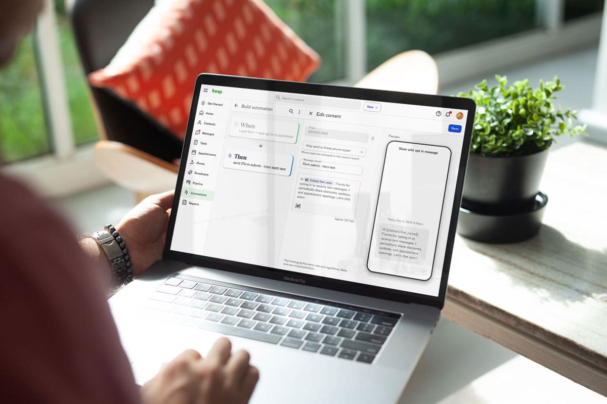 Person using a MacBook Pro to build an automation workflow in Keap CRM software, with a plant and window light in the background.