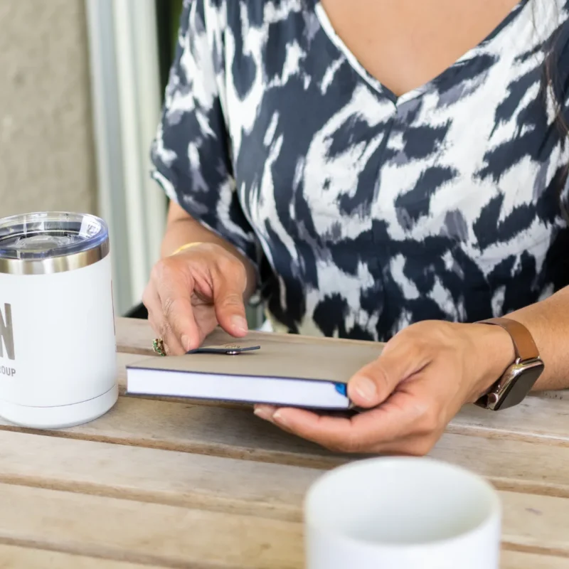 A lady sitting on a chair with her book in hand, cup of coffee and cup of water next to her | Social Media’s Impact