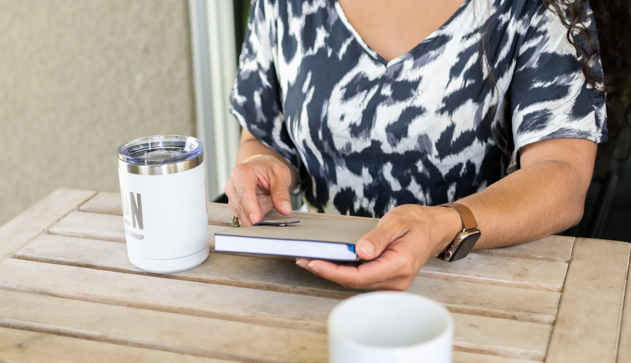 A lady sitting on a chair with her book in hand, cup of coffee and cup of water next to her | Social Media’s Impact