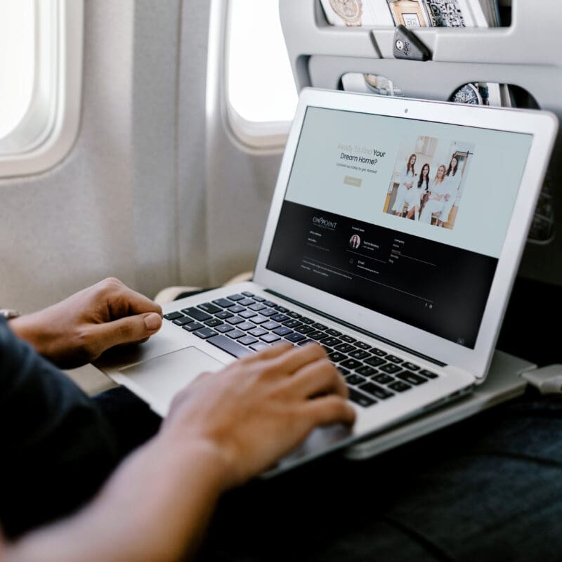 Person using a laptop on an airplane with a real estate website open, symbolizing remote work and website accessibility from anywhere.