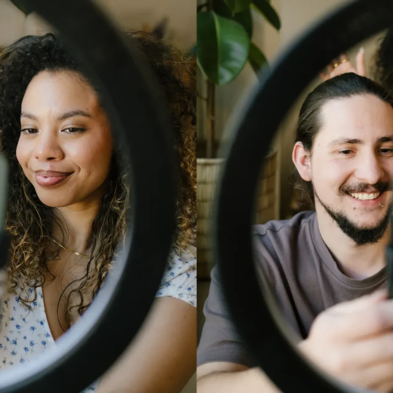 Two images side by side. On the left, Inhouse Designer, Talana , taking a selfie on a Light stand. On the Right, Jnr Social Media Manager Jacques, also taking a selfie on a light stand with Talana in the background. Both of them trying to master the Social Media algorithms
