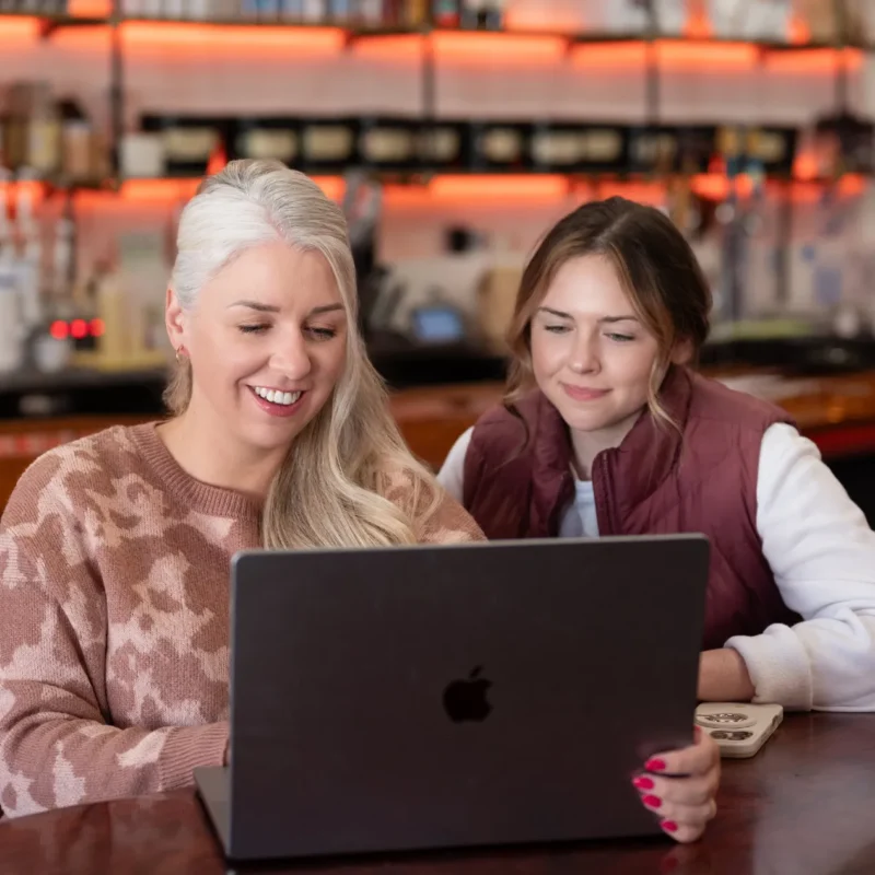 Two women reviewing content together on a laptop in a relaxed workspace setting