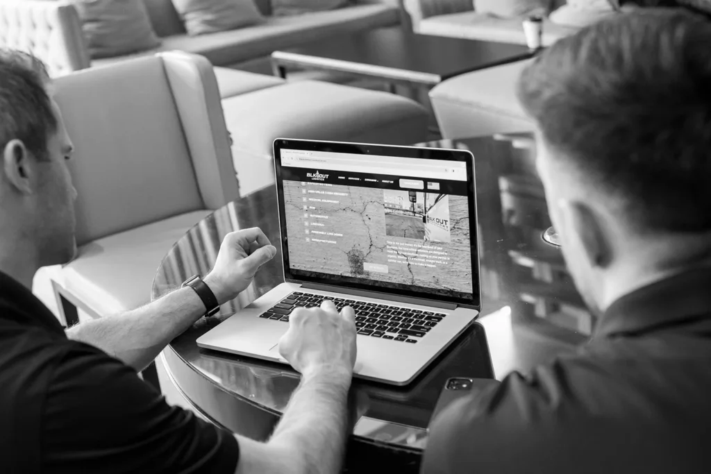 Website Review During Client Strategy Meeting Two professionals reviewing a website on a laptop during a collaborative business meeting