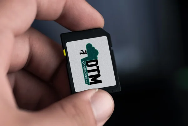 DTM Consulting LLC logo displayed on a small electronic device held between fingers