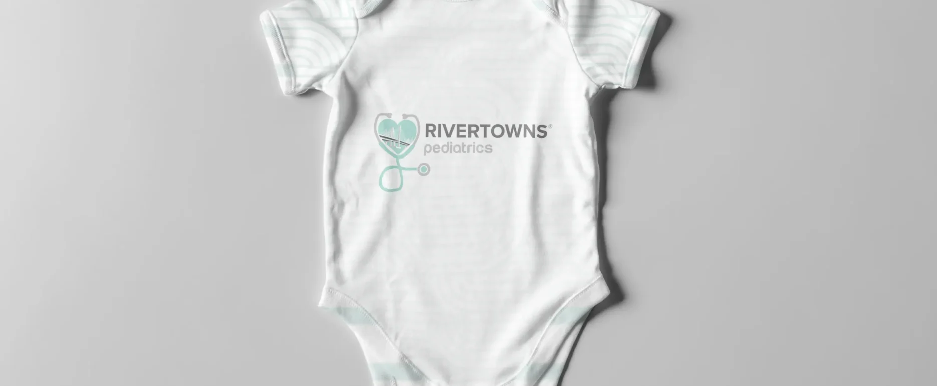 Rivertowns Pediatrics branded baby onesie with heart stethoscope logo