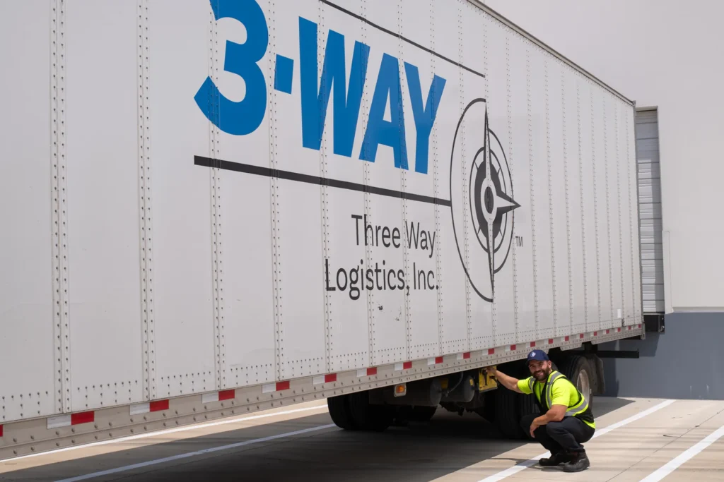 Three Way Logistics Branded Trailer at Distribution Facility Logistics worker inspecting a Three Way Logistics branded semi trailer at a loading dock