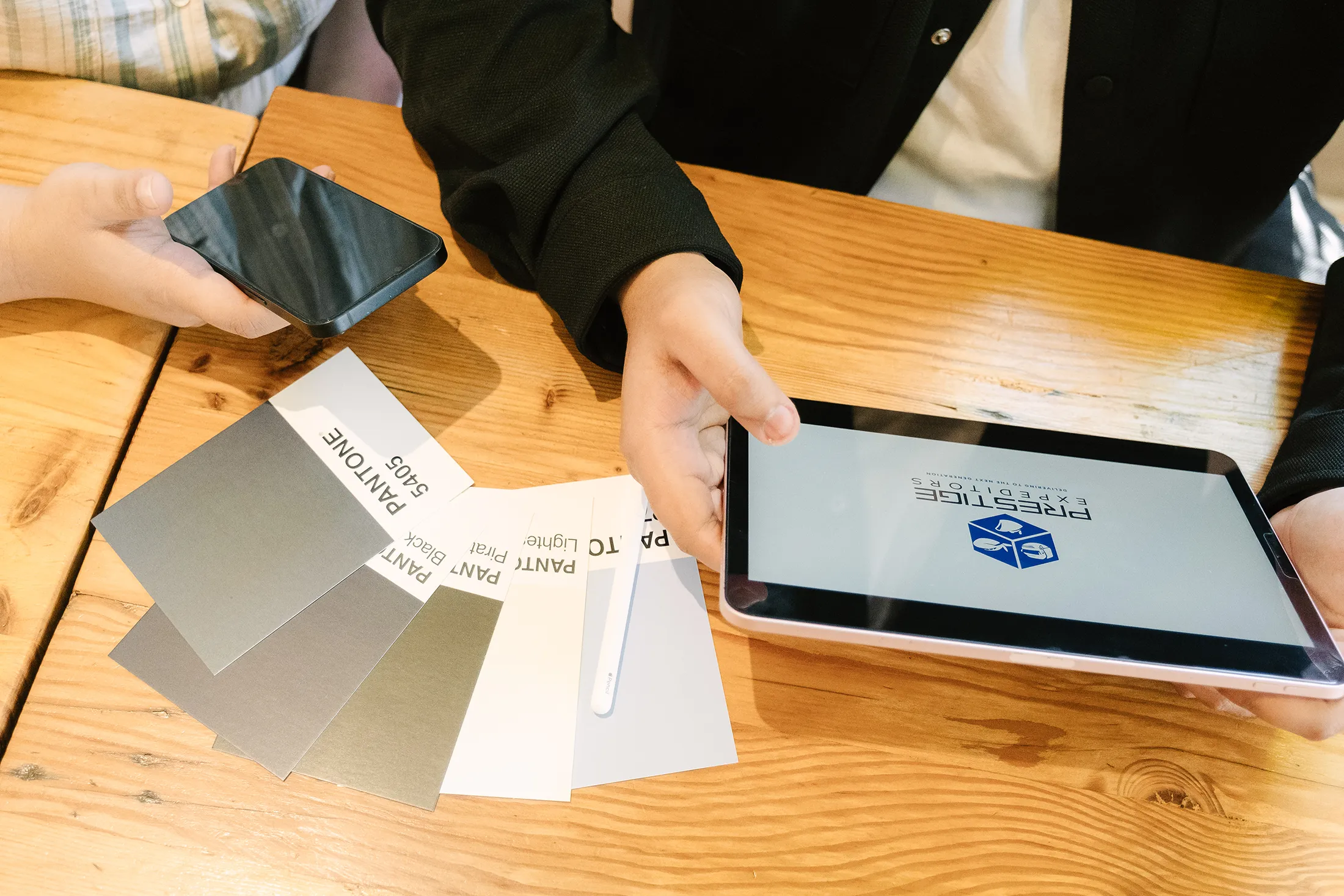 Hands reviewing brand design materials, including color swatches and a tablet displaying a logo, during a brand identity planning session.