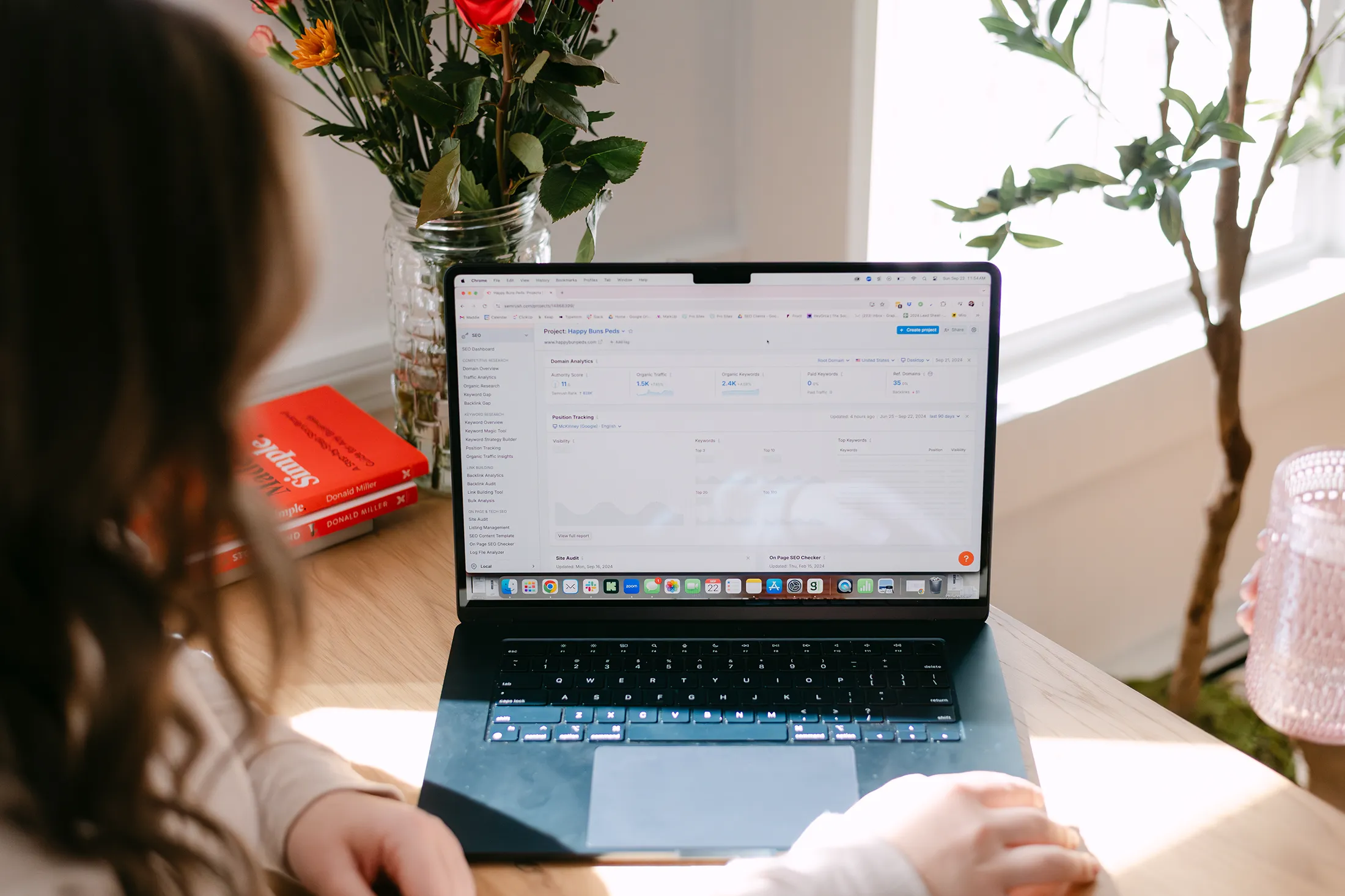 Person reviewing SEO analytics and keyword performance dashboard on a laptop at a home office desk with flowers and books.